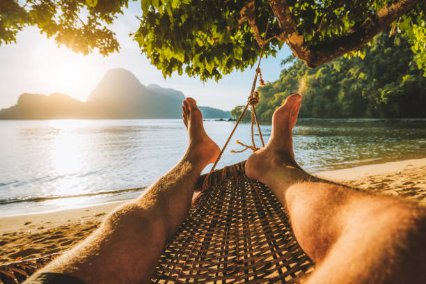 Feet of adult man relaxing in a hammock on the beach during summer holiday Feet of adult man relaxing in a hammock on the beach during summer holiday. el nido photos stock pictures, royalty-free photos & images
