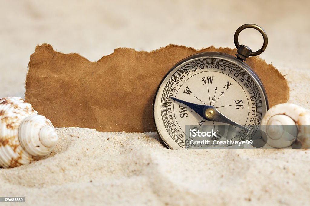 Vacation destination Compass on sand with seashells and blank torn paper. Animal Shell Stock Photo