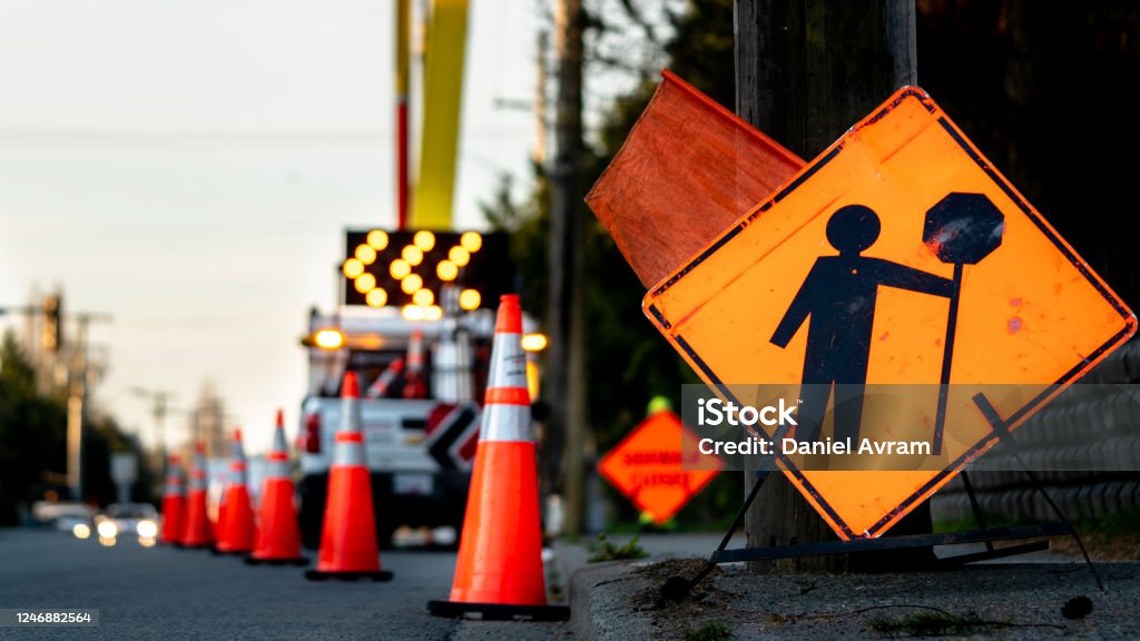 Lane closure on a busy road due to maintenance signs detour traffic temporary street work orange lighted arrow, barrels, and cones. Road Construction Stock Photo