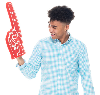 Front view of aged 18-19 years old with curly hair generation z teenage boys fan - enthusiast standing in front of white background wearing rolled-up sleeves who is showing cool attitude and cheering who is pointing and holding foam hand