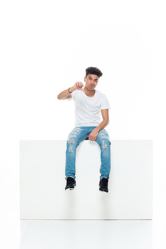 Full length of aged 18-19 years old with curly hair generation z teenage boys resting in front of white background wearing shirt who is feeling sad and showing thumbs down