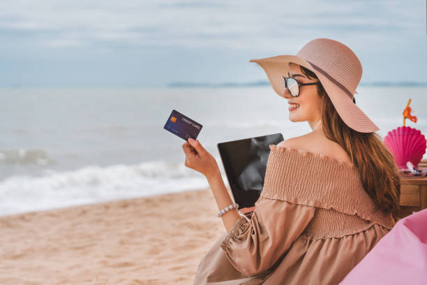 Asian woman holding credit card for online shopping at the beach. On vacation at Pattaya beach, asian traveler woman with floppy hat use credit card in luxury cafe. exclusive travel stock pictures, royalty-free photos & images