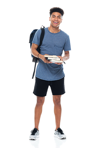 Full length of aged 18-19 years old with curly hair generation z teenage boys student standing in front of white background wearing backpack who is studying and holding bag