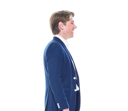 Side view of aged 20-29 years old caucasian young male in front of white background wearing blazer who is smiling with hand by side