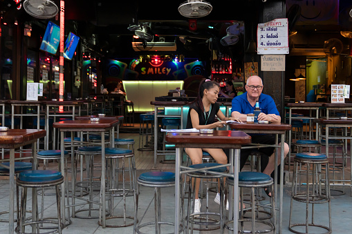 Thailand, Phuket, March 30, 2020:an elderly European man drinks beer with a Thai woman in a bar on Bangla road. Street photos, real life .