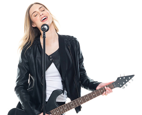 Waist up of aged 20-29 years old who is beautiful with long hair caucasian female singer dancing in front of white background wearing leather jacket who is excited and holding microphone and using audio equipment