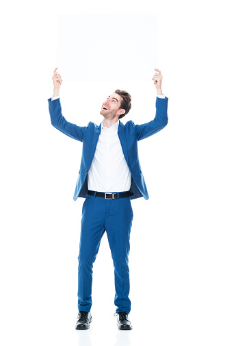One person of aged 30-39 years old with brown hair caucasian young male business person standing in front of white background wearing shirt who is happy who is showing with hand and holding banner sign with copy space