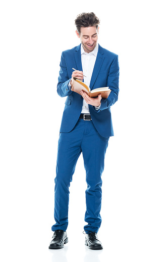 Front view of aged 30-39 years old with brown hair caucasian male businessman standing in front of white background wearing shirt who is laughing who is writing and holding book and using pen