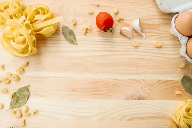 Photo of Cooking food background with free space for text. Composition with pasta, tomato, eggs, garlic, bay leaf over the wood background. Ingredients for cooking with copy space. Top view with copy space