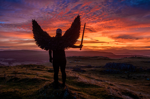 A lone Black Winged Warrior Angel holding a sword overlooking beautiful British landscape at dawn