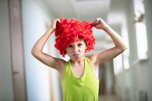 A child in a bright wig. Funny boy with red artificial hair. Do not like the hairstyle .