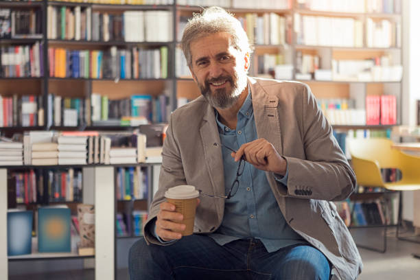 istock Senior man in a bookstore sitting on a chair drinking coffee looking at camera 1246929861