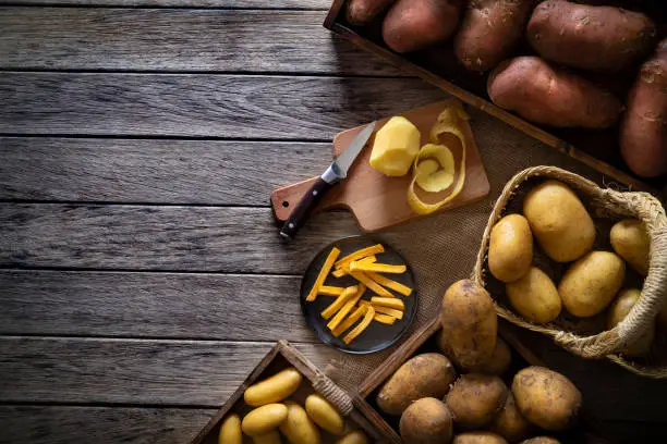 French fries potatoes on a rustic wooden board table with raw potatoes around of different colors and sizes shapes
