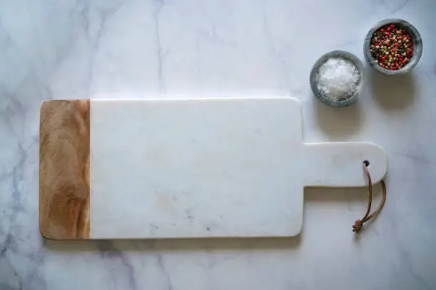 White Marble cutting board on white marble counter with salt and pepper spices monochromatic kitchen food background with copy space