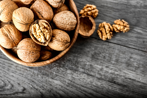Whole walnuts on dark board, Walnut kernels in wood rustic bowl. top view. Helathy raw food concept.