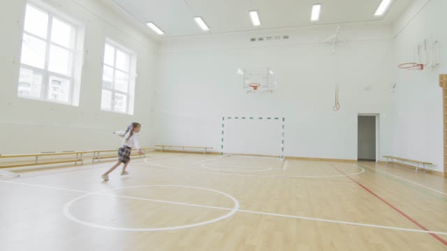 little girl running in the school gym. A girl who does not play sports. Happy schoolgirl in the gym