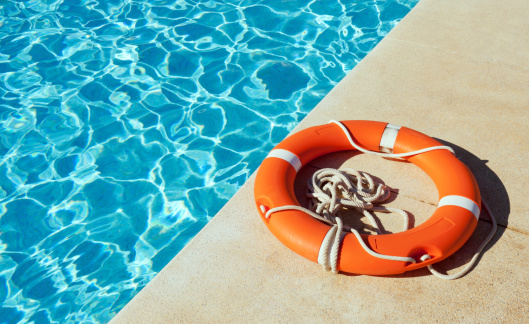 A life preserver lying at the side of an outdoor swimming pool.