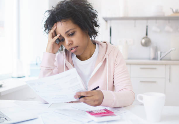 ラップトップで台所のテーブルに座っているアフリカ系アメリカ人女性を動揺させ、住宅ローンの負債のために財政的ストレスやプレッシャーに対処し、心配したり不安を感じたりしました� - paperwork emotional stress women document ストックフォトと画像