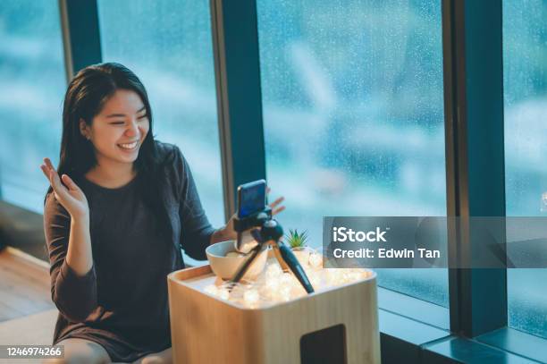 An Asian Chinese Teenager Girl Vlogging In Her Room Eating Apple Using Her Smart Phone During Raining Day Smiling Stock Photo - Download Image Now