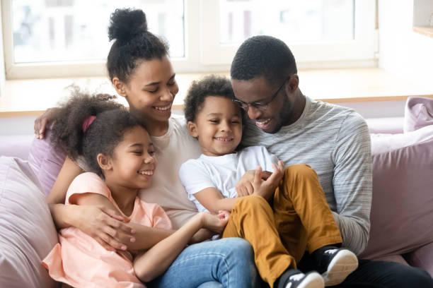 padres africanos con niños divirtiéndose sentados en el sofá interior - happy time fotografías e imágenes de stock