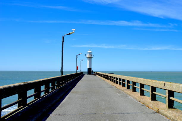Blankenberge on a sunny afternoon. Lighthouse at the end of a walking tarmac road, a concrete construction pier above the sea.