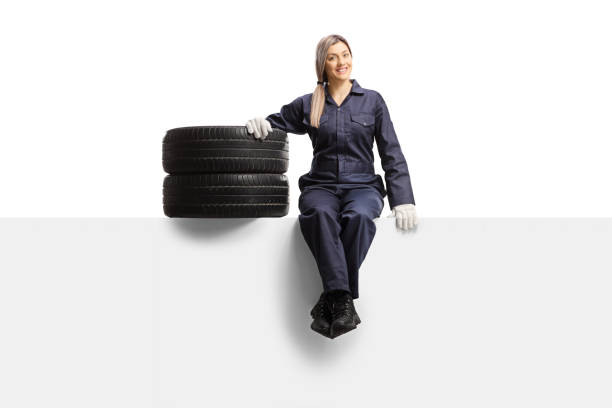 istock Female auto mechanic worker in a uniform sitting on a panel with tires and looking at the camera 1246992291