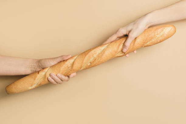 istock Two women's hands hold a French baguette on a light background 1247008880