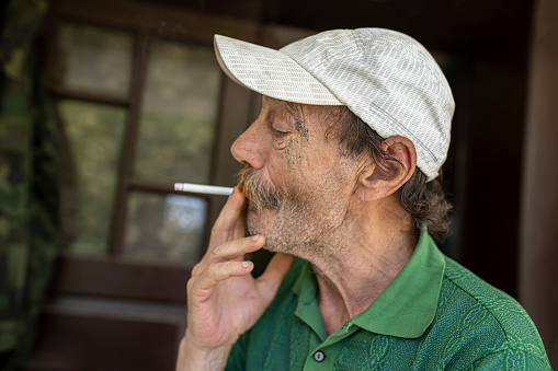 One senior man in green shirt is smoking cigarette.