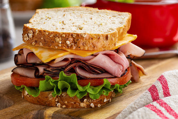 Ham and Cheese Sandwich on Whole Grain Bread Ham sandwich with cheese, tomato and lettuce on whole grain bread on a wooden cutting board sandwich stock pictures, royalty-free photos & images