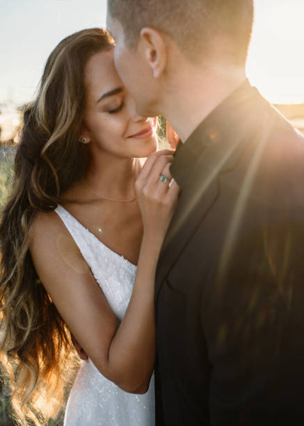 sensual pareja de bodas abraza. guapo novio besa suavemente a su hermosa novia con el pelo ondulado en la luz del sol de oro. - jewelry ring luxury wedding fotografías e imágenes de stock