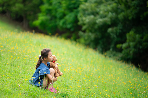 Girl sitting with a teddy bear in the flower garden