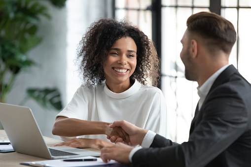 Smiling African American businesswoman advisor broker shaking client customer hand at meeting, making great deal after successful negotiations, executive mentor greeting new worker intern