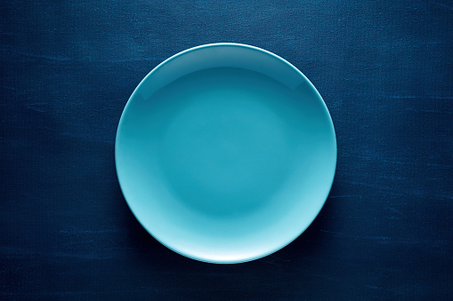 One empty blue round plate or dish on blue background with copy space.