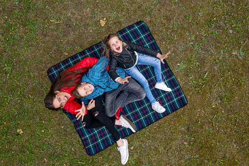 view from above of a happy family sitting on a checkered blanket in the forest plain, looking up and and waving a hand