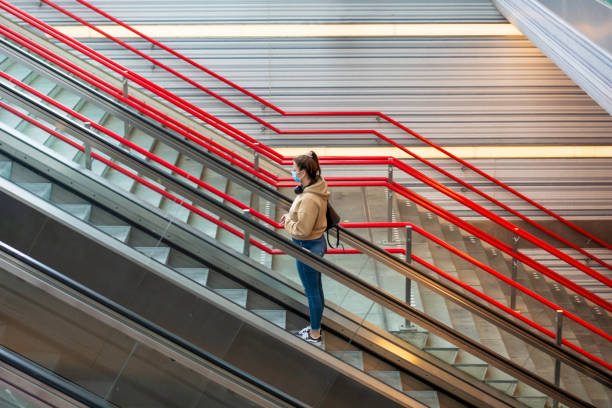 une jeune femme portant le masque protecteur et se tenant sur l’escalator dans la gare pendant l’éclosion de coronavirus covid-19. - subway station railroad station netherlands subway photos et images de collection