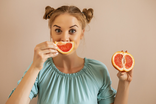 Portrait of cute woman holding slices of grapefruit