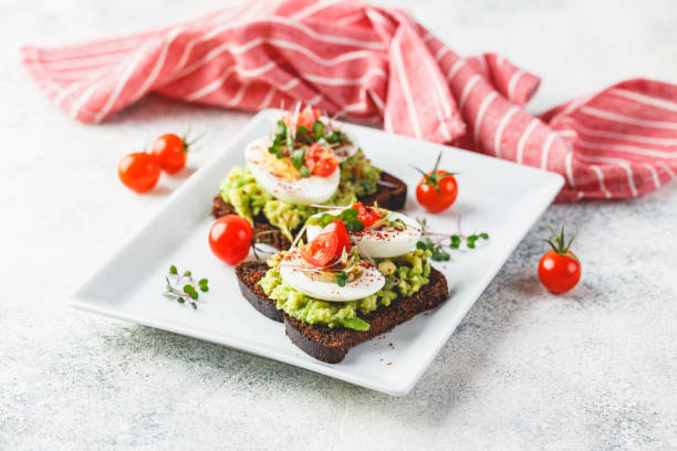 Toast with avocado and egg Healthy toast on rye bread with avocado, boiled eggs, spices, cherry tomatoes and microgreen on plate. Delicious appetizer, snack. egg cherry tomato rye stock pictures, royalty-free photos & images