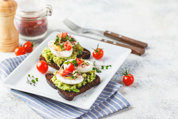 Toast with avocado and egg Healthy toast on rye bread with avocado, boiled eggs, spices, cherry tomatoes and microgreen on plate. Delicious appetizer, breakfast or snack. egg cherry tomato rye stock pictures, royalty-free photos & images