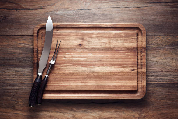 Empty vintage wooden cutting board with roast knife and fork on wooden table