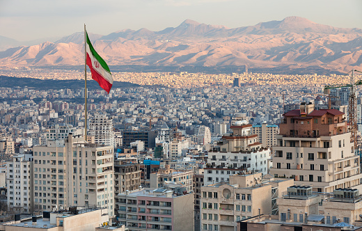 Vista aérea del horizonte de Teherán al atardecer con la gran bandera de Irán ondeando en el viento photo