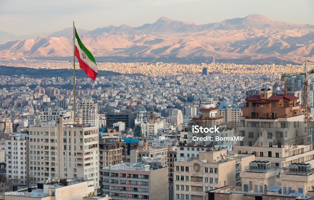 Aerial view of Tehran Skyline at Sunset with Large Iran Flag Waving in the Wind Waving Iran flag above skyline of Tehran at sunset. Iran Stock Photo
