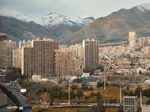 Skyline of Tehran and waving Iran flag against snow covered Alborz Mountainswith Instagram warm effect.