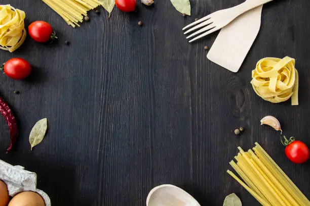 Photo of Cooking food background with free space for text. Composition with spaghetti, tomato, eggs, garlic, bay leaf over the wood background. Ingredients for cooking with copy space. Top view for the design