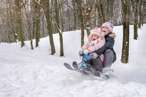 kinder schlittenfahren. ein kleines mädchen und ein junges mädchen genießen ihr los auf dem schlitten. - little boys sled clothing slide stock-fotos und bilder