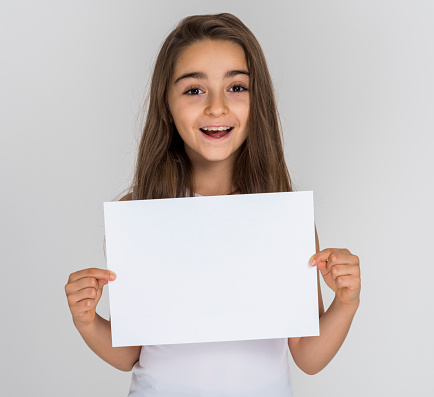 Cute teenage girl holding a white empty placard (for you to copy space) over white background