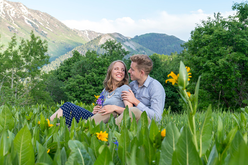 This is view of a young couple stopped for a romantic moment in a grassy mountain meadow and reclining among wildflowers.  They look adoringly at each other as they enjoy the views. This picture was taken near Buffalo Peak, part of the Wasatch range that overlooks Provo, Utah.