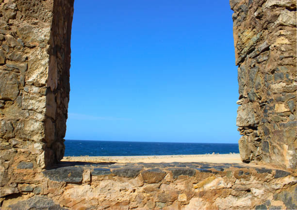 The ruined window in ruins. The view overlooks the ocean. Visible water and sand. On the sides are old stones folded into the window frame. Aruba, August 2014