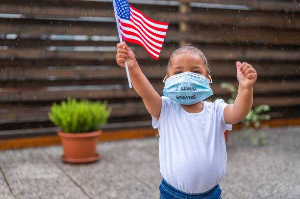 little cute girl wearing protective face mask with 'i wanna breathe' handwriting on it and holding a small american flag - child flag fourth of july little girls imagens e fotografias de stock