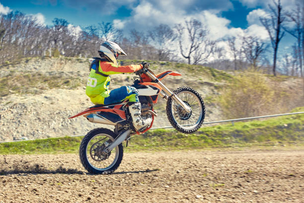 motocross, a rider stands on the rear wheel of a bike, riding on the rear wheel. extreme, industrial, motorcycle cross-country riding for extreme - motorcycle biker riding motorcycle racing imagens e fotografias de stock