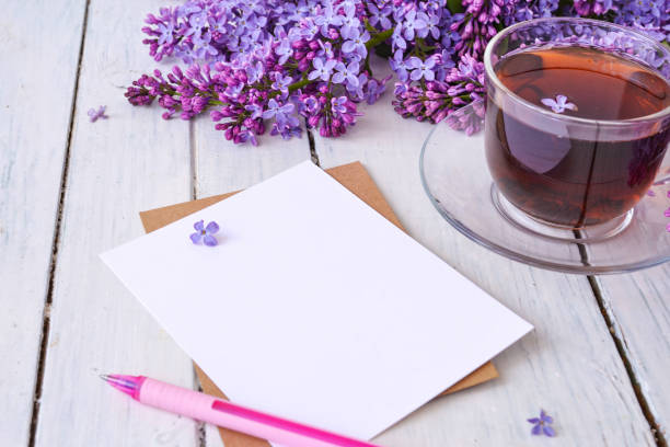 Cup of tea with lilac flowers on a wooden white background. Nearby lies a sheet of paper, and a pink pen. Mocap for postcards. Spring time. Vase with lilacs. Copy space for text. The concept of holidays and good morning wishes. taza de té con flores lilas sobre fondo blanco de madera. cerca se encuentra una hoja de papel, y un bolígrafo rosa. mocap para postales. hora de primavera. jarrón con lilas. copiar espacio para texto. el concepto de vacaciones y buenos deseos de la ma�